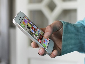 man with a light blue sweatshirt holding a cellphone with apps on the screen