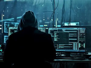 man with hoodie working and a desk with several monitors